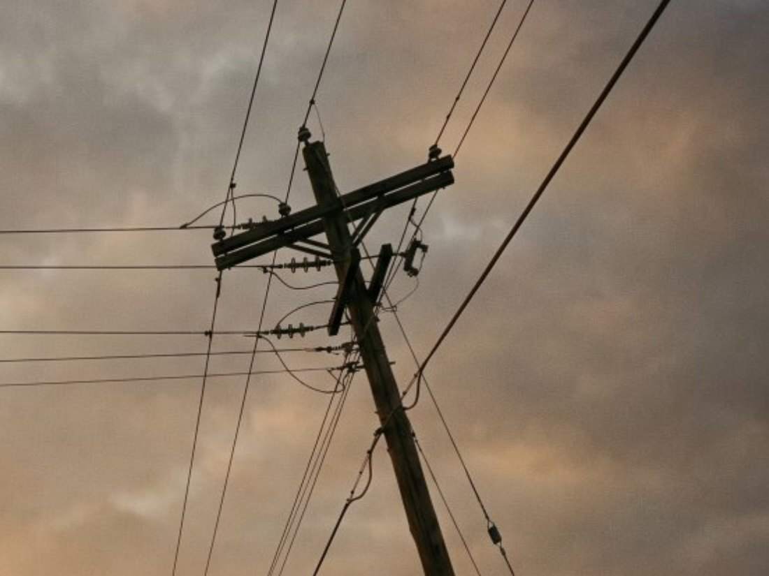 Crossarm and insulators of a utility pole against a dawn sky