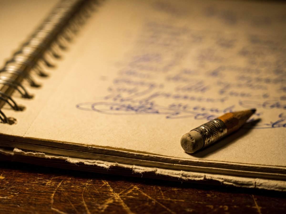 Handwritten lyric notes in a worn spiral notebook with a stub pencil